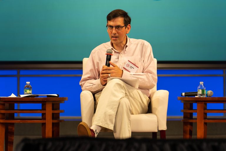 photo of Eugene Sonn seated on a stage holding a microphone
